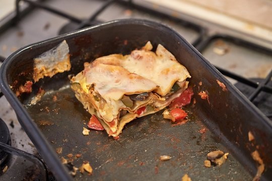 Lasagne leftover food in a pan on a dirty kitchen stove