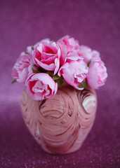 Beautiful little pink flowers in a small vase with a pattern on a dark pink shiny background