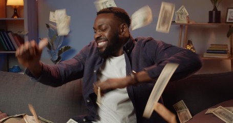 Happy afro american man holding smartphone and making successful deal while working from home. Young guy winning big money and rejoicing. Money falling from above - Powered by Adobe