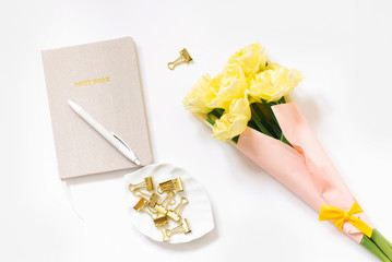 Office Desk with a notebook, yellow flowers, clips, white pen with dots for paper on a white background. The view from the top. Workplace of a female freelancer or blogger