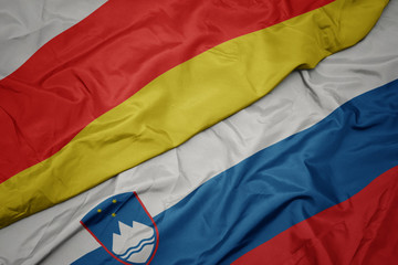 waving colorful flag of slovenia and national flag of south ossetia.