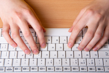 two female hand is typing on a white keyboard with English letters. The concept of home schooling, distance learning
