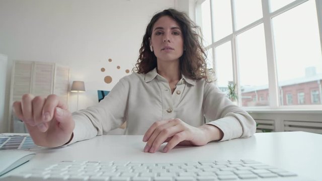 Vertical portrait of beautiful Caucasian businesswoman with curly hair wearing glasses staying home and discussing business strategy with colleagues by video link