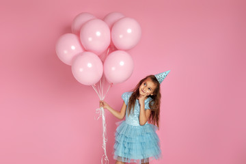 adorable smiling little child girl in blue dress and birthday hat with pastel pink air balloons thinking about something on pink background. birthday party.