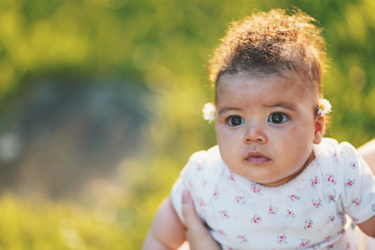 Beautiful interracial baby portrait looking front during sunset wearing 4 months to 6 month baby suit. Green grass backgrounds and sun that comes from the back of the baby. 85mm lens photography