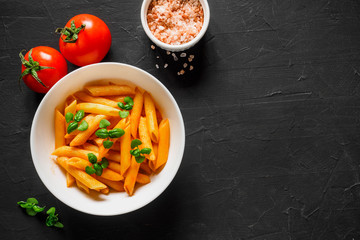 Pasta Penne in tomato sauce Pomodoro, garnished green basil leaves on black table. Traditional italian food. Copy space, top view