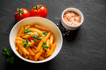 Pasta Penne in tomato sauce Pomodoro, garnished green basil leaves on black table. Traditional italian food. Copy space, top view