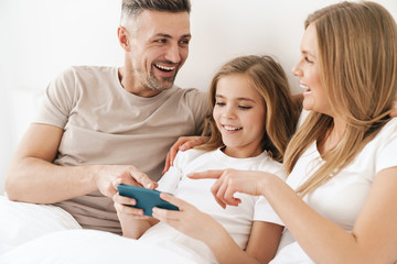 Photo of girl playing video game on cellphone with parents in bad