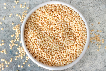 Uncooked millet in white ceramic bowl on metal background view from above
