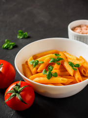 Pasta Penne in tomato sauce Pomodoro, garnished green basil leaves on black table. Traditional italian food. Copy space