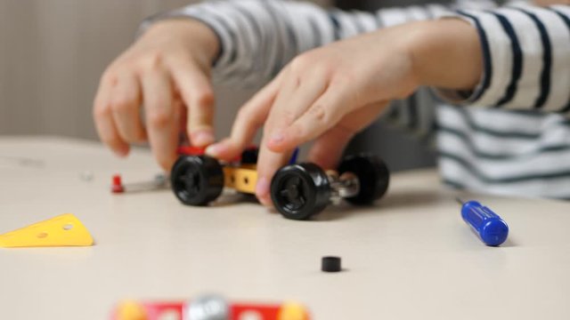 A pre-school boy spends time playing a game of constructor. A smart, thoughtful child builds a car model by twisting the parts. Happy childhood, development, distance learning.