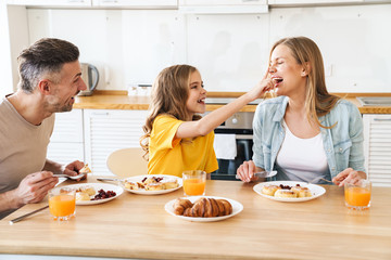 Photo of funny family laughing while having breakfast in kitchen - obrazy, fototapety, plakaty