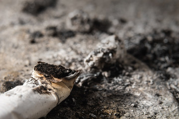 FOCUS ON THE CIGARETTE BUTT. Smoked cigarette on the ashtray with ashes around. Cigarette butt and ashes background.