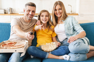 Photo of cheerful family eating popcorn and pizza while watching tv