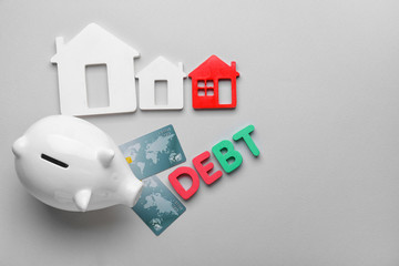 Credit cards with piggy bank, models of houses and word DEBT on grey background