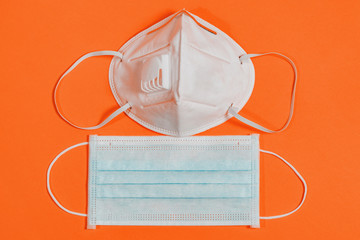 Medical mask with valve and surgical mask on orange background. Two masks of different shapes one above the other.