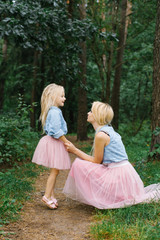 A mother and a five-year-old daughter in the same romantic clothes are walking in the Park or in the woods.They talk and talk about something. Mother's day