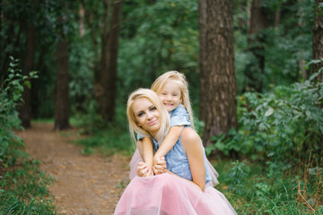 Obraz na płótnie Canvas A mother and a five-year-old daughter in identical pink tulle skirts and blue denim shirts are walking in the Park or in the woods. The daughter hugs her mother. Mother's day
