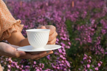 Female holding coffee or tea cup in hand on flowers garden location.