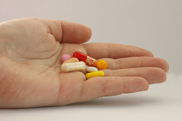 Tablets of different colors and shapes lie in palm of your hand. Palm of the whole. Tablets of red, white, yellow, pink. Located on the left. Taking drugs. Treatment. Home first aid kit. Copy space