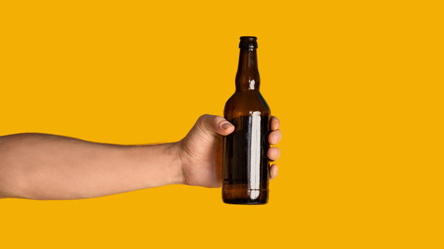 Male hand holding bottle of refreshing beer on orange background, mock up for design. Panorama