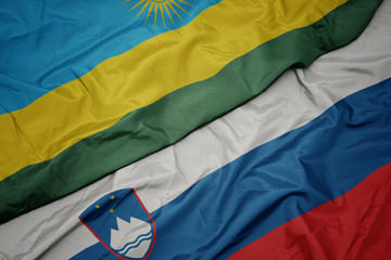 waving colorful flag of slovenia and national flag of rwanda.