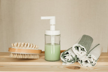 soap dispenser on a wooden shelf next to folded towels and artificial flower, sauna accessories