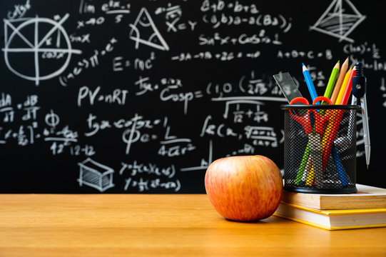 Education background concept. Stationery in holder color pencil, compasses tool, scissors, rulers, sharpener with apple On chalkboard with the Mathematical formula.
