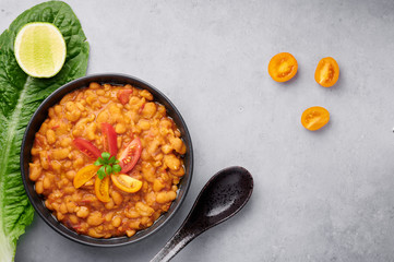 Ful Medames or Fava Beans in black bowl at grey backdrop. Foul Mudammas is a Egyptian, Lebanese, Syrian, Eritrean, Israeli cuisines breakfast dish of cooked beans with cumin, tomatoes, parsley
