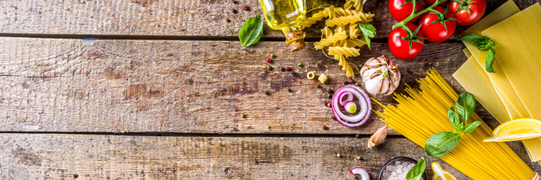 Assortment set of various raw pasta and condiments. Cooking italian pasta concept with fresh herbs and vegetables. Rustic style, wooden background top view copy space
