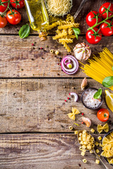 Assortment set of various raw pasta and condiments. Cooking italian pasta concept with fresh herbs and vegetables. Rustic style, wooden background top view copy space