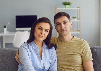 A couple in a serious emotional mood with problems looks at the camera while sitting on the couch.
