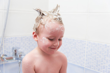Cute baby washes his hair in the bath.