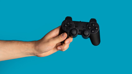 Stay home hobby. Millennial guy holding video game controller on blue background, closeup. Panorama © Prostock-studio