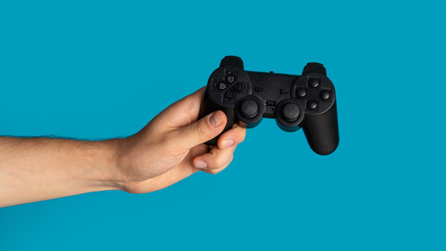 Stay home hobby. Millennial guy holding video game controller on blue background, closeup. Panorama