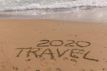 summer beach with 2020 travel lettering on sand near sea