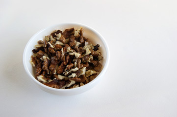 Peeled walnuts in a white cup on a white table