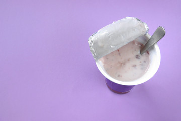 A pink yogurt with strawberry in an open plastic cup on pink background.