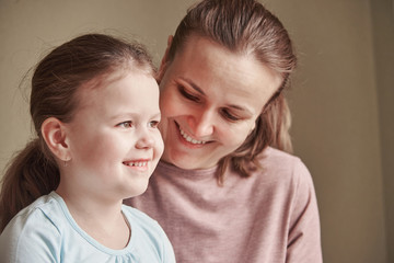 A charming little girl and her beautiful young mother use a digital tablet and smile while sitting on chairs at home