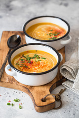 Pumpkin cream soup. Roasted pumpkin and carrot puree soup with turmeric, cream, paprica, chives and pumpkin seeds on grey background. Vegetarian and Vegan recipe. Green living. Organic food.