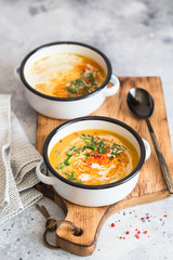 Pumpkin cream soup. Roasted pumpkin and carrot puree soup with turmeric, cream, paprica, chives and pumpkin seeds on grey background. Vegetarian and Vegan recipe. Green living. Organic food.