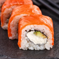 Philadelphia sushi rolls with salmon and cream cheese and avocado on a black slate plate close up.