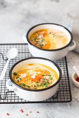 Pumpkin cream soup. Roasted pumpkin and carrot puree soup with turmeric, cream, paprica, chives and pumpkin seeds on grey background. Vegetarian and Vegan recipe. Green living. Organic food.