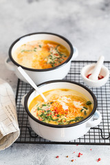 Pumpkin cream soup. Roasted pumpkin and carrot puree soup with turmeric, cream, paprica, chives and pumpkin seeds on grey background. Vegetarian and Vegan recipe. Green living. Organic food.