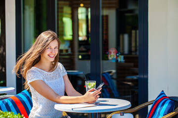 Young beautiful brunette woman with a cold drink sitting in a cafe on the street
