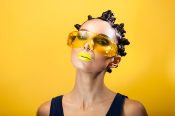 portrait of a girl on a yellow background with the original creative afro hairstyle in the form of horns, in yellow construction glasses looks at the camera