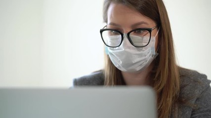 Young woman working at laptop computer in office mask during epidemic covid-19 - Powered by Adobe