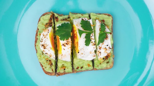 Eating cuted avocado toast with poached egg, spices and cilantro leaf. Loop stop motion animation. Healthy food background. Tiffany blue plate, top view.