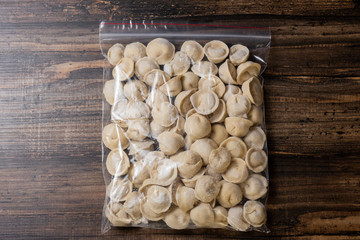 Frozen dumplings with meat in batter in a plastic bag on a wooden background