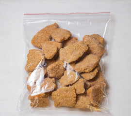 Frozen nuggets in batter in a plastic bag on a white wooden background